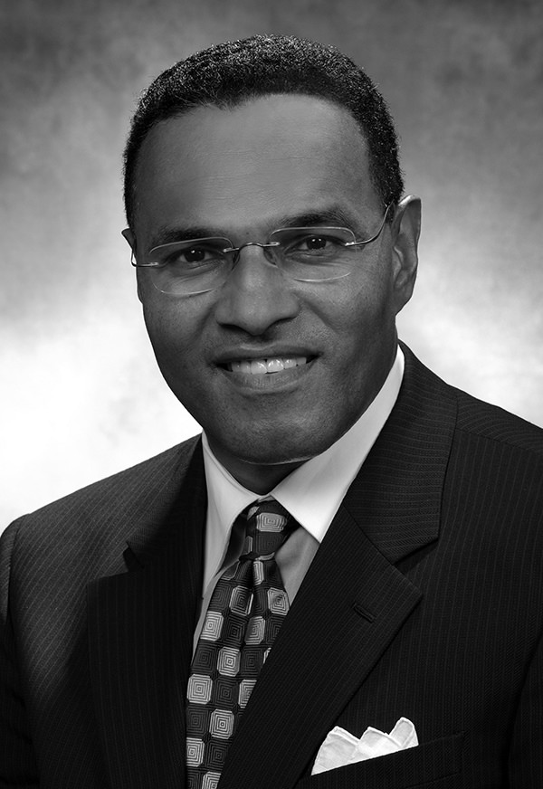 A black and white portrait of Freeman Hrabowski. He is wearing a suit and tie and glasses,